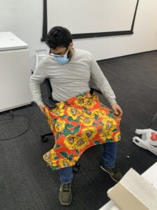 Nafl trying on a prototype he created. He is testing the velcro straps by affixing the prototype to the arm rest of a chair.