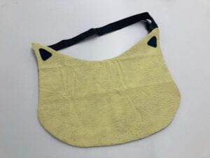 Tammy mat with a greenish-yellow felt front and a buckled strap. The mat resembles an apron in the shape of a cat's face. At the top of the mat the two sides of the strap are sewn to the cat ears.