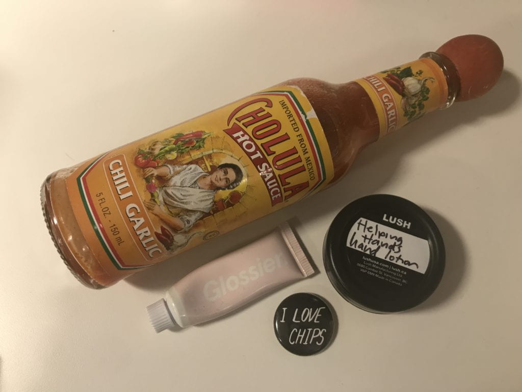 Photograph of hot sauce, lip gloss, hand lotion, and pin