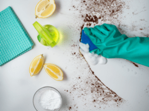 hand wearing dishwasher glove scrubbing dirt of a table with water, lemon, and baking soda