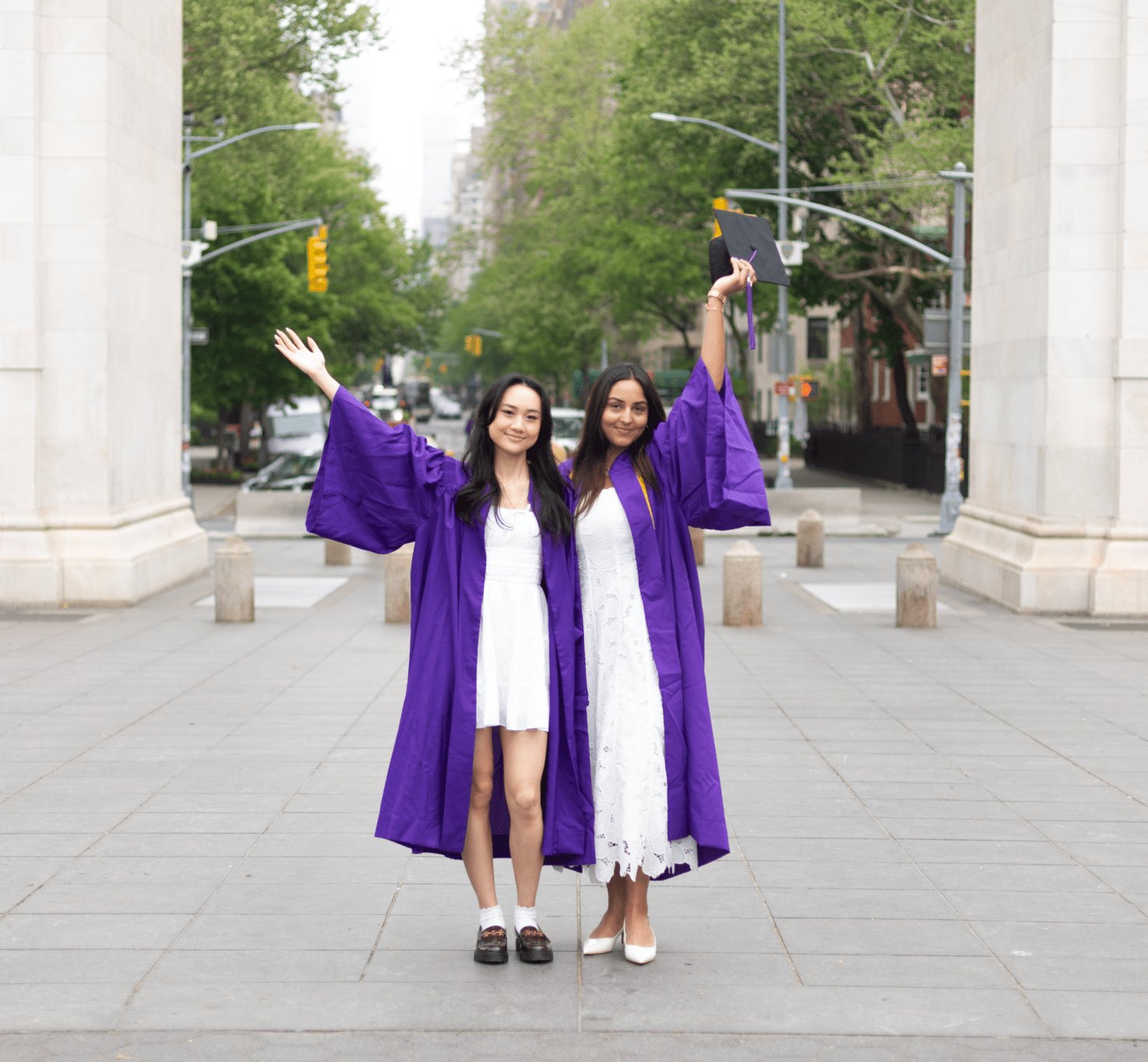 Two students in their graduation gowns posing in front of the arch