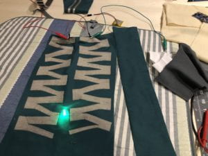 Conductive fabric cut in a zig zag pattern is used to bring power to a green LED light