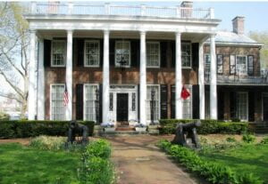 picture of a large house with 6 white columns. 2 cannons are flanking the walkway up to the house.