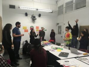 Image of a classroom with students standing around a table discussing and gesturing