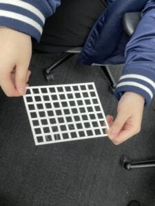 Two hands holding a slanted rectangular piece of plastic with rhombi-shaped holes