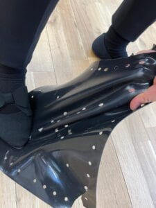 Black boot and hand stretching a black sheet of silicone rubber with holes