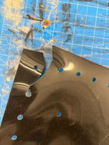 Black silicone rubber sheet with holes that have a tear at the corner, on top of a blue mat