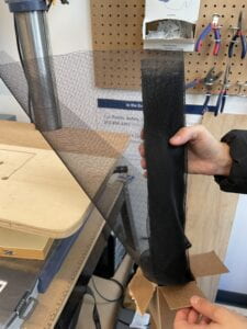 Two hands holding a roll of black nylon mesh with small holes