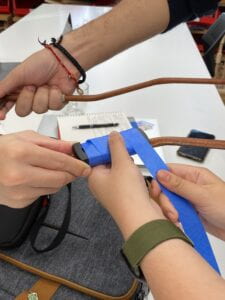 The image shows three people using blue tape to attach the Fidlock socket onto the harness handle