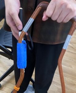 A member of the group holds the harness handle in their left hand, imitating its orientation when attached to a guide dog's harness. The Fidlock twist socket is attached to the right leg of the handle, facing the user. This orientation of the socket would allow the user to pull the cane away from the handle.