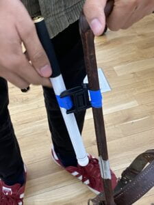 A group member holds up the harness handle and cane attached by the Fidlock slide magnet. Unlike the last photo, the two sides of the magnet are attached with tape -- velcro could not fasten the magnets tightly enough. 