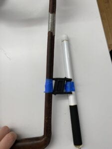 The harness handle and cane connected by magnets lay flat against the table. The cane leans slightly crooked, suggesting that the tape is not enough to fasten the magnet.