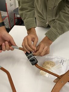 A group member closes a zip tie around the Fidlock Twist socket and harness handle while another member holds the harness as they work over a table.