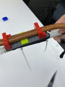 A group member holds up a cane with the Fidlock Twist's plugs using a pair of arch-shaped Legos attached to a Twist-sized Lego base.