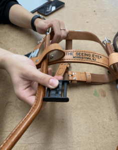 Two hands hold up the the handle of a harness lying on a table. Between the thumb and forefinger wrapped around the handle, the slider varient is lined up parallel.