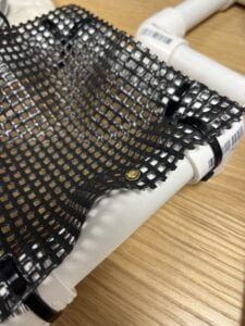 A golden metal screw fastening trampoline mesh onto PVC tube