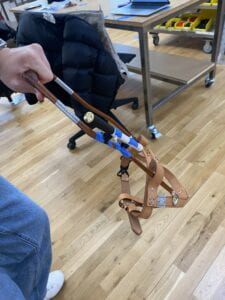 A group member holds up a harness with a cane attached to one of its arms by a pair of Fidlock snap magnets. The two snaps are arranged so that a user can release the case by pulling it up.