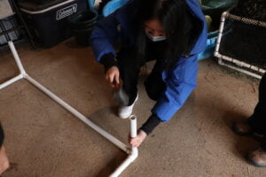 A young woman hitting a PVC leg into a rectangular PVC frame with a mallet