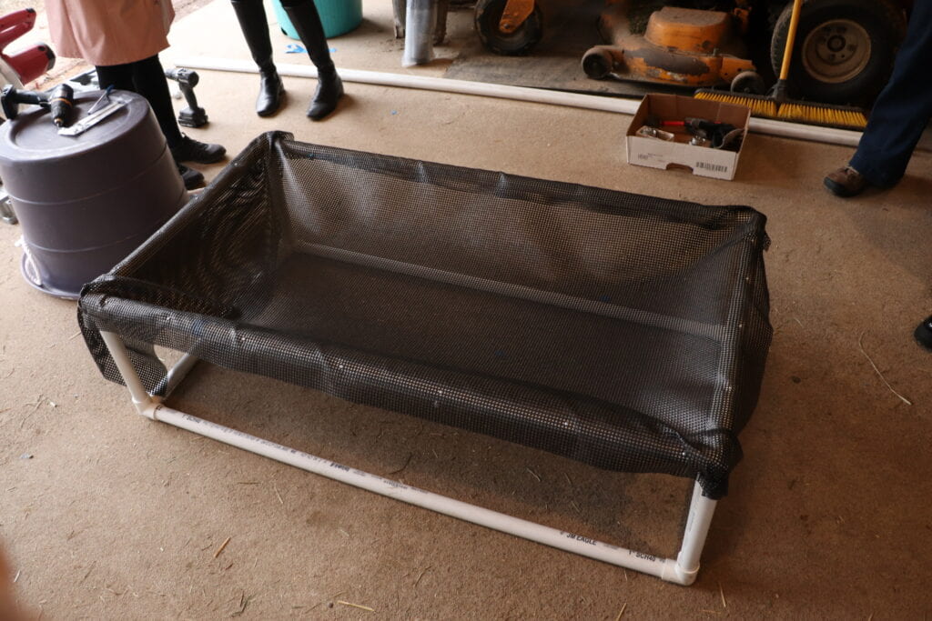 A PVC cuboid cot with trampoline mesh fastened on the top base with nails