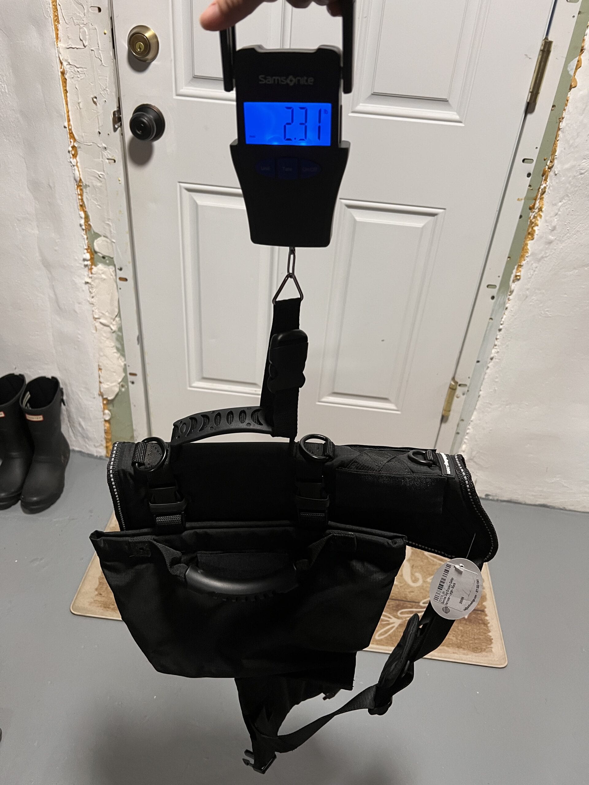 An image of the bag with adaptations being weighed with a second scale to ensure reliability. The scale is attached to the handle and it measures the weight as the bag is lifted in the air. The scale says 2.31 lbs.