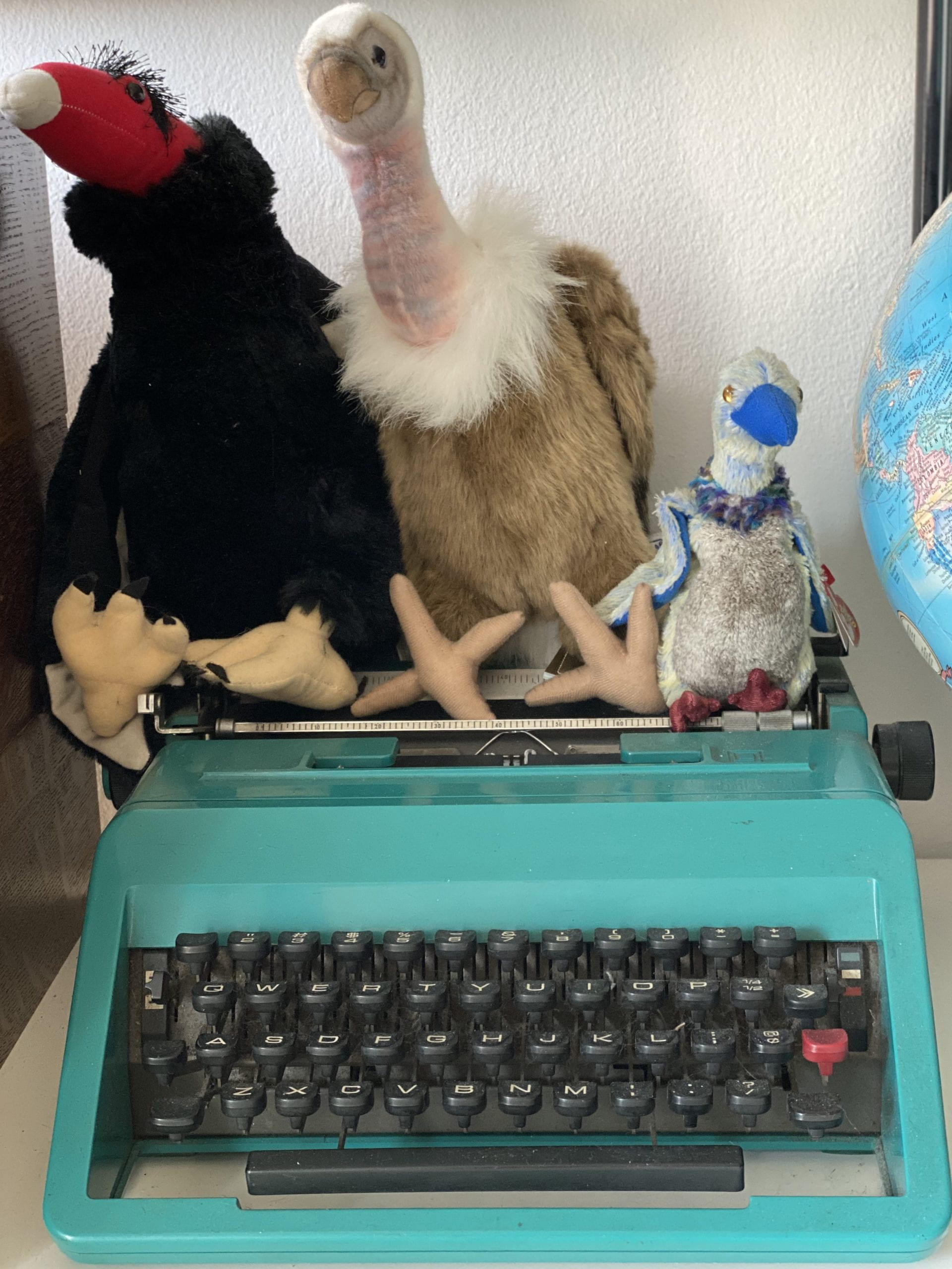 Three buzzard stuffed animals sitting on top of a teal typewriter.