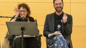 MAGE DESCRIPTION: On the left, Dr. Simi Linton, a white woman in a wheelchair with curly hair adjusts her glasses, smiling. On the right, Dr. Kevin Gotkin, a bearded white man laughs, mid-finger- snap. Simi and Kevin are co-directors of the Disability Arts/NYC, affiliated with the NYU Center for Disability Studies, which sponsored this 2018 event where they discussed their work developing disability arts in the city, co-sponsored by the Departments of Performance Studies, Art and Public Policy and the Hemispheric Institute of Politics and Performance.