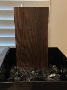 black box full of black crystal rocks with a dark brown wood standing up