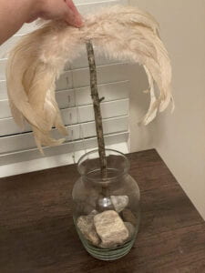 feathery wings being held on top of a wooden stick sitting in a glass vase of rocks