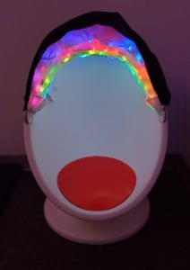 An egg-shaped chair with a red cushion inside and a shade that is black on the outside and has colorful LED lights on the inside.