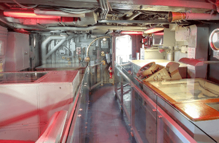 Exhibit pathway through the Flag Bridge inside of the Intrepid. There are exposed pipes and plotting tables covered in glass for protection.