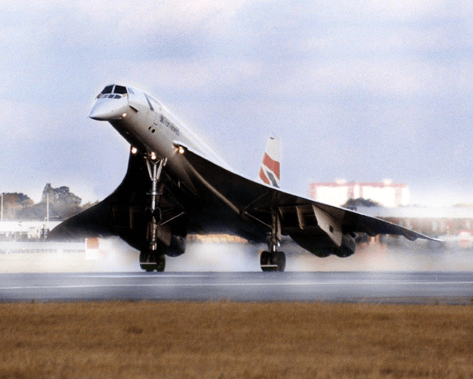 Front view of a Concorde as it lands on the rear wheels of its landing gear. The plane is tilted up, with the front wheel still in the air, and the nose cone tilted down.