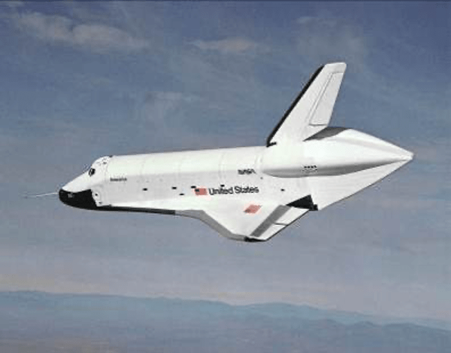 View of the space shuttle orbiter Enterprise with its tail cone on, from its left side as it glides toward the left of the frame over a hilly landscape.