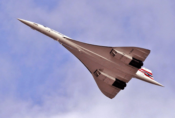 A Concorde flies directly overhead, toward the top left corner of the frame. It is pointed at the front and its triangular delta wings extend out starting a quarter of the way from the front.