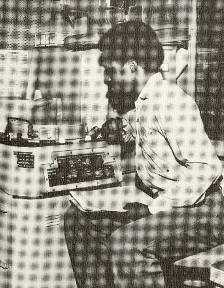 Black and white image of a man seated and looking at radar equipment, holding papers in his left hand