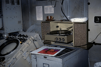 Colored image of record player and records placed on top of a filing cabinet, next to a radar set with round screen