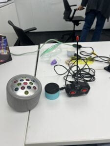 An image of a round grey toy with rainbow lights and the toy's controller with the adapted button to controller it. 