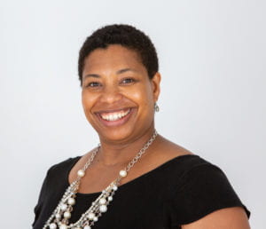 Headshot of Regine Gilbert smiling against white background wearing a black shirt.