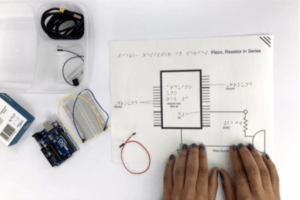 Two hands touching a tactile schematic for a microprocessor with Arduino components nearby. 