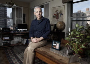 Allan Goldstein at home leaning on a bench near a picture of his brother. 