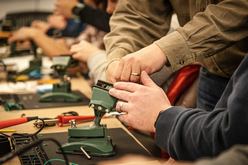 Josh Miele's hands guide an attendee with securing their circuit board in their vice.