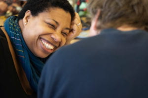 Regine, one of the volunteers, faces one of the attendees smiling widely, her head tilted to the side, propped up on her hand.