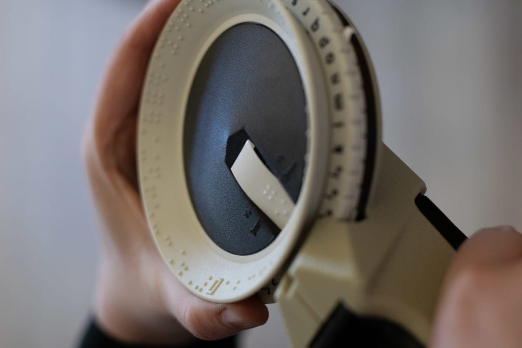 Close up of hands rotating a Braille labeler to create a beverage label.