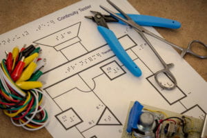 A tactile schematic of a continuity tester with alligator clips, a wire cutter, forceps, and the finished project laying around its perimeter.