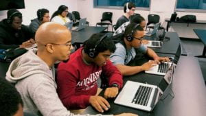 A diverse group of Tech Kids Unlimited students sitting at laptops in a classroom. 