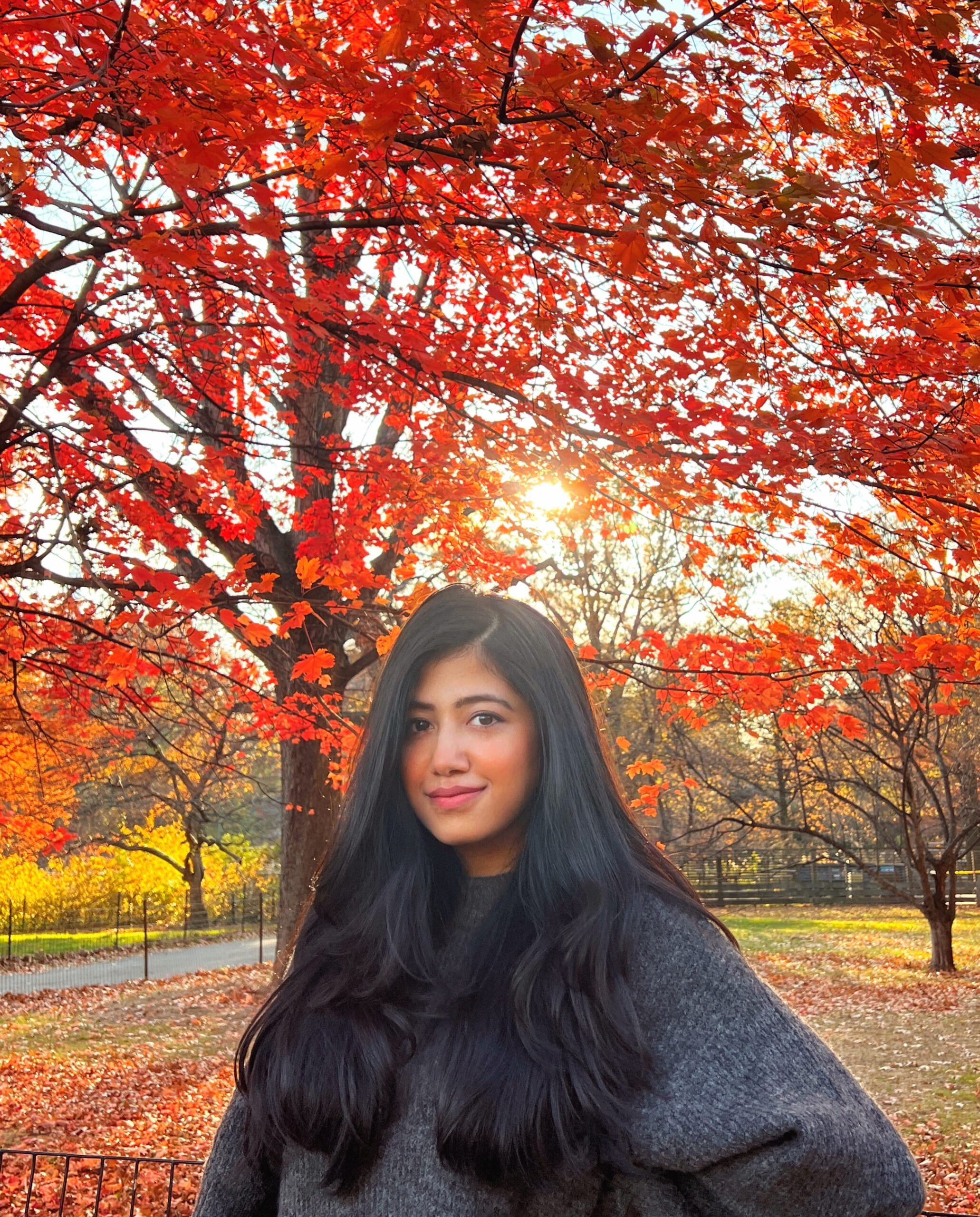 Photo of Spandita, smiling, standing in a park in front of a tree that has red leaves