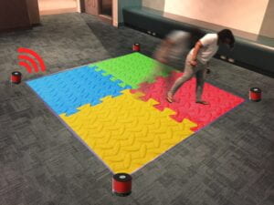 A mat split into four sections with a speaker at each corner and a person walking toward one corner.