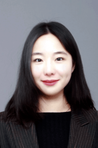 Asian female in her 20s with black long straight hair wearing a greyish brown jacket, smiling in front of the camera