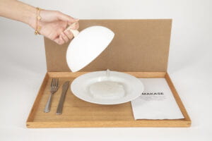 Hand lifting a plate cover on a multisensory tangible interface that subverts the omakase experience