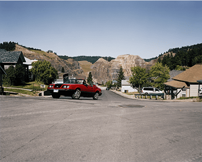 Image of a red car driving up a hill. 