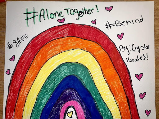 Drawing of a rainbow submitted by Crystal. Surrounding the rainbow are hearts and hashtags with sayings such as be kind, alone together, and safe.